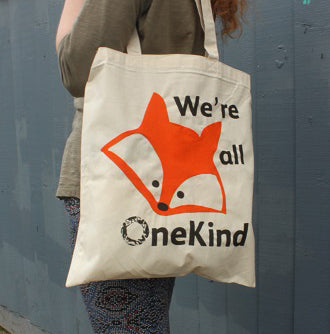 Girl standing with organic canvas shopping bag with fox head image and slogan 'We're all OneKind'.