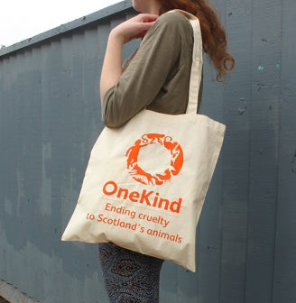 Girl standing with organic canvas shopping bag with OneKind logo and strapline.